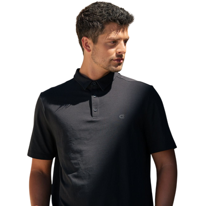 A person with short, light brown hair is wearing the Men's Everyday Polo by Cozy Earth in a light gray shade, paired with light beige pants. They are standing and slightly looking over their left shoulder with a neutral expression against a plain white background. |Color:Stone