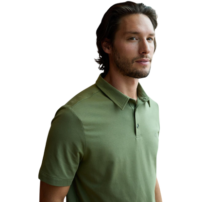 A person with short, light brown hair is wearing the Men's Everyday Polo by Cozy Earth in a light gray shade, paired with light beige pants. They are standing and slightly looking over their left shoulder with a neutral expression against a plain white background. |Color:Stone