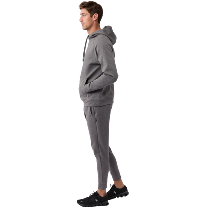 A person wearing the Men's StretchTech Hoodie from Cozy Earth, paired with matching gray pants, stands against a plain white background. The hoodie features drawstrings and a front pocket. The individual is looking forward with a neutral expression. |Color:Coal Heather