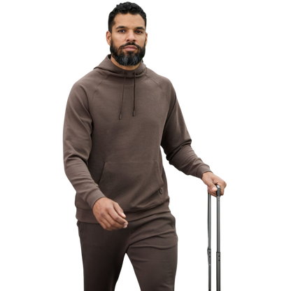 A person wearing the Men's StretchTech Hoodie from Cozy Earth, paired with matching gray pants, stands against a plain white background. The hoodie features drawstrings and a front pocket. The individual is looking forward with a neutral expression. |Color:Coal Heather