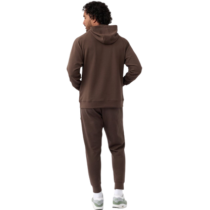 A person wearing the Men's StretchTech Hoodie from Cozy Earth, paired with matching gray pants, stands against a plain white background. The hoodie features drawstrings and a front pocket. The individual is looking forward with a neutral expression. |Color:Coal Heather