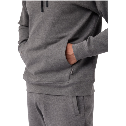 A person wearing the Men's StretchTech Hoodie from Cozy Earth, paired with matching gray pants, stands against a plain white background. The hoodie features drawstrings and a front pocket. The individual is looking forward with a neutral expression. |Color:Coal Heather