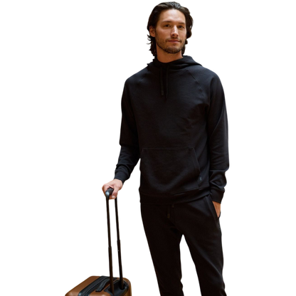 A person wearing the Men's StretchTech Hoodie from Cozy Earth, paired with matching gray pants, stands against a plain white background. The hoodie features drawstrings and a front pocket. The individual is looking forward with a neutral expression. |Color:Coal Heather