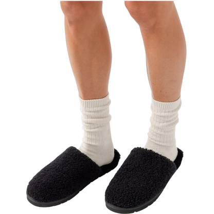 Close-up of a person's lower legs wearing white crew socks and Cozy Earth's Puffy Sheep Slipper, which are black and fuzzy. The background is plain white. |Color:Black Sheep