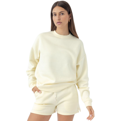 A woman with long brown hair wears a Cozy Earth Women's CityScape Crewneck and matching shorts against a plain white background. She has a neutral expression and keeps one hand in her pocket. |Color:Lemonade