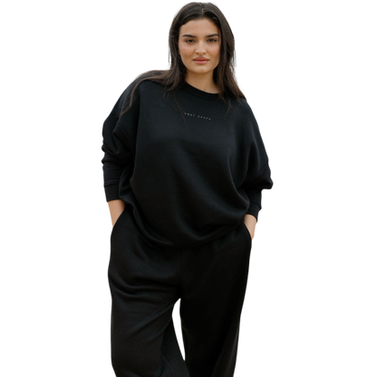 A person with curly hair models the Cozy Earth Women's CityScape Crewneck and matching pants in light pink against a plain white backdrop. |Color:Peony