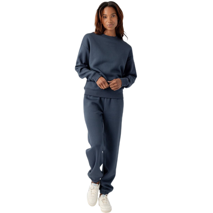A person with curly hair models the Cozy Earth Women's CityScape Crewneck and matching pants in light pink against a plain white backdrop. |Color:Peony