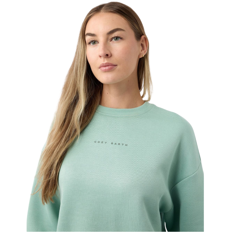 A person with curly hair models the Cozy Earth Women's CityScape Crewneck and matching pants in light pink against a plain white backdrop. |Color:Peony