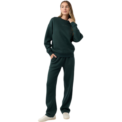 A person with curly hair models the Cozy Earth Women's CityScape Crewneck and matching pants in light pink against a plain white backdrop. |Color:Peony