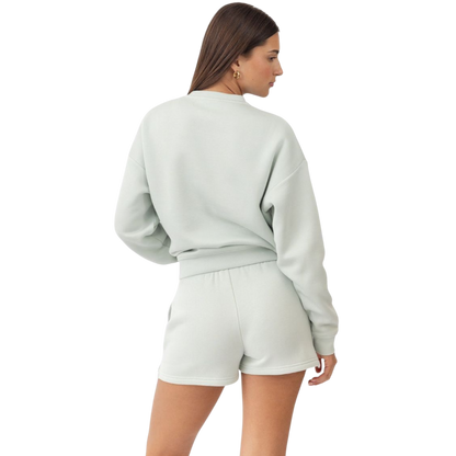 A person with curly hair models the Cozy Earth Women's CityScape Crewneck and matching pants in light pink against a plain white backdrop. |Color:Peony