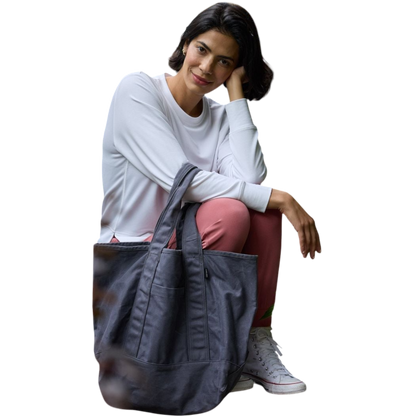A person with long black hair is standing against a plain white background, wearing a Cozy Earth Women's StudioLite Crewneck in light green and dark green pants. They are looking down with a gentle smile, gently touching their neck with one hand. |Color:Haze