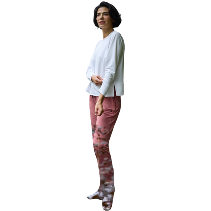 A person with long black hair is standing against a plain white background, wearing a Cozy Earth Women's StudioLite Crewneck in light green and dark green pants. They are looking down with a gentle smile, gently touching their neck with one hand. |Color:Haze